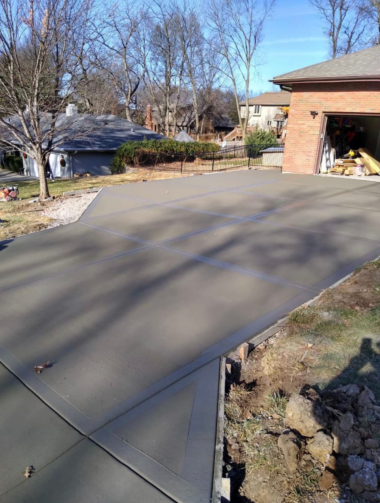 Large new concrete driveway at a brick home with a black iron fence along the property line