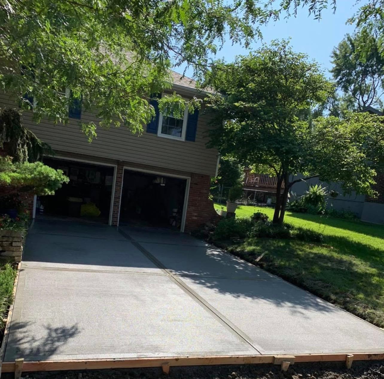 New concrete driveway leading to a two-car garage, shaded by mature trees