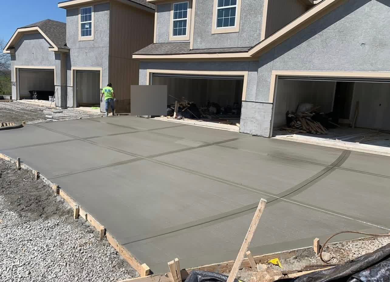 RK Deluxe crew member finishing a large new concrete driveway pour across multiple garage bays at a new-construction townhome building