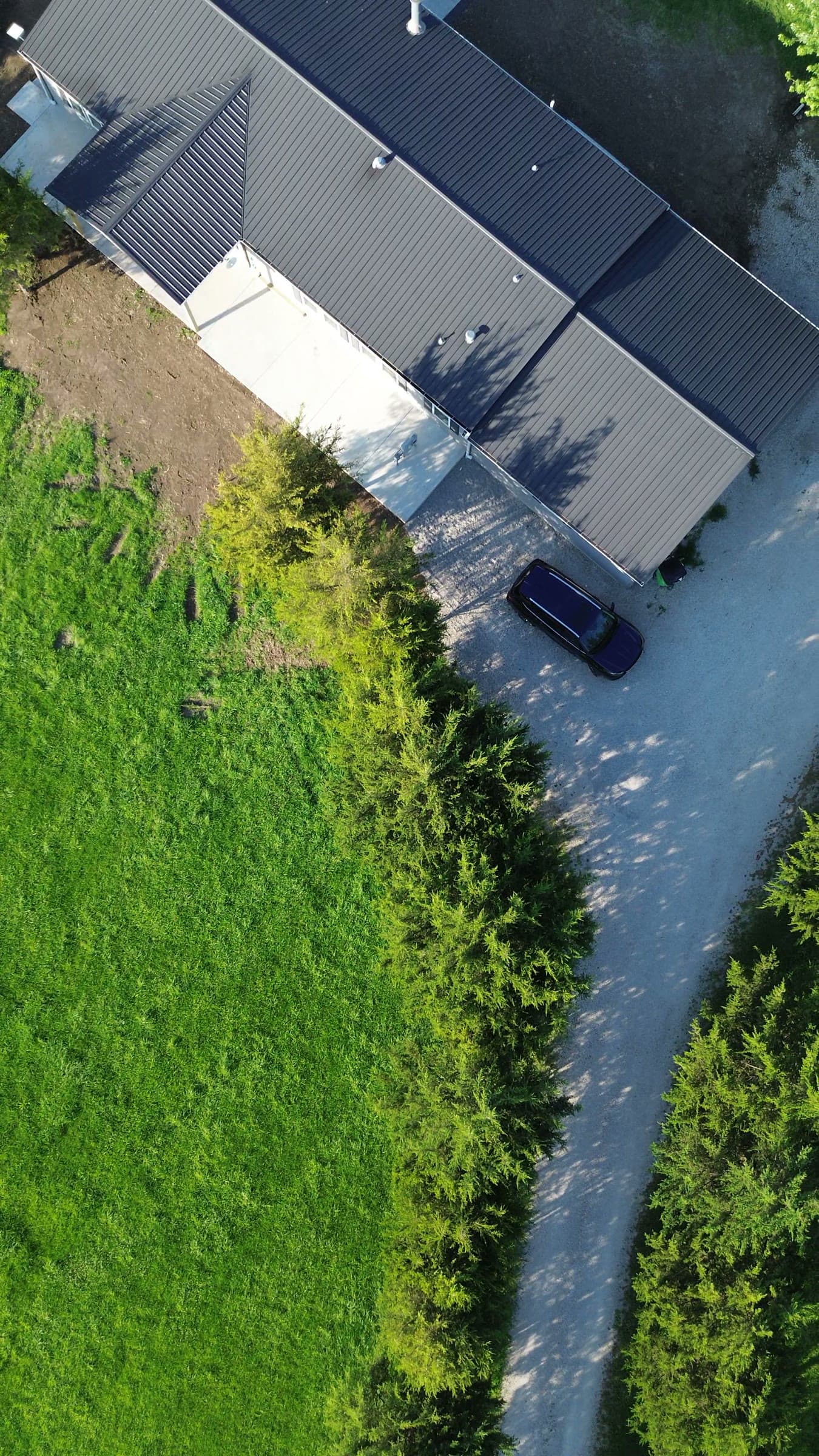 Top-down aerial drone view of the same rural property's metal roofline, driveway, and surrounding tree line