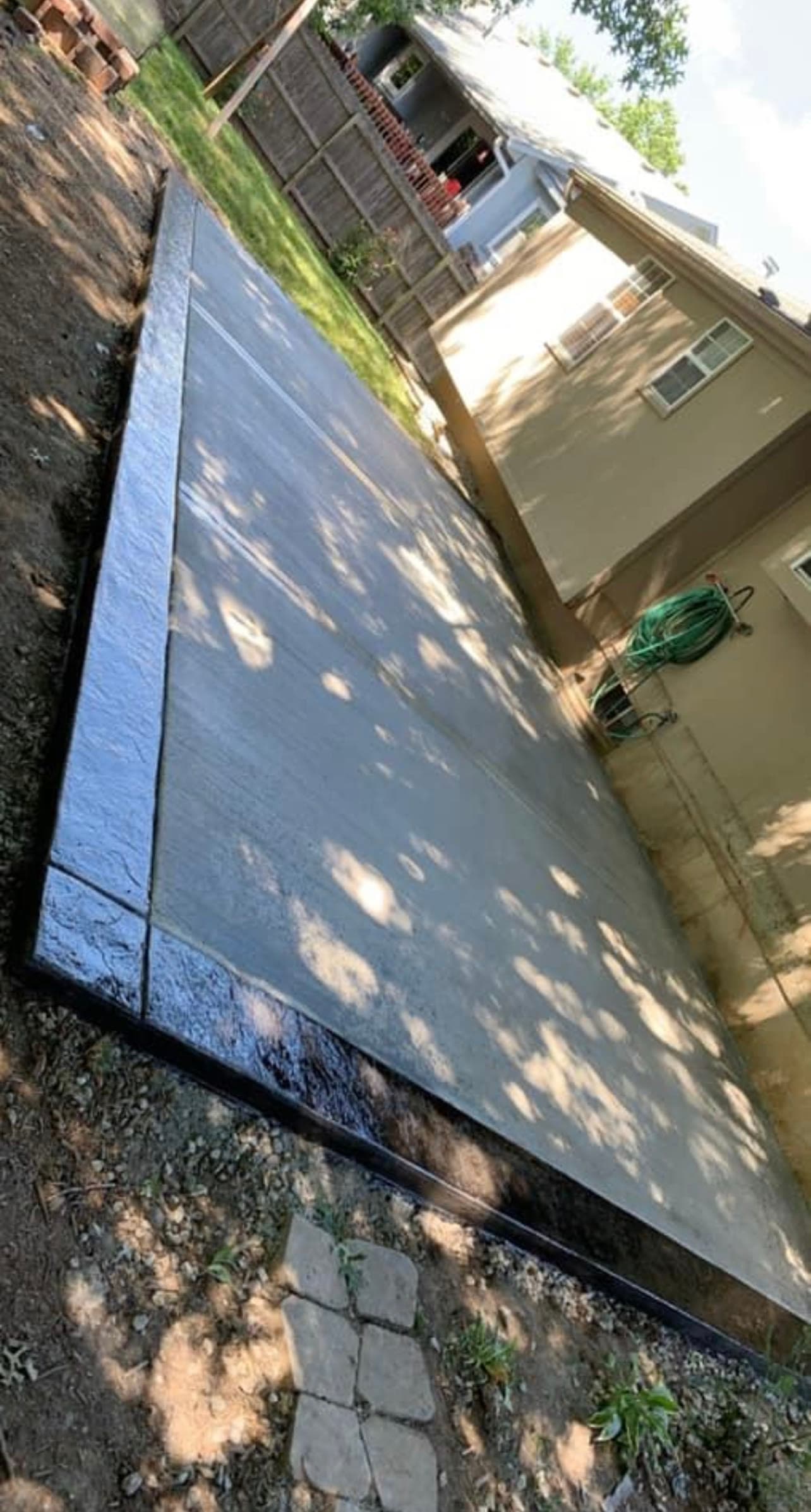 New concrete patio slab in a backyard, dappled tree shade across the finished surface