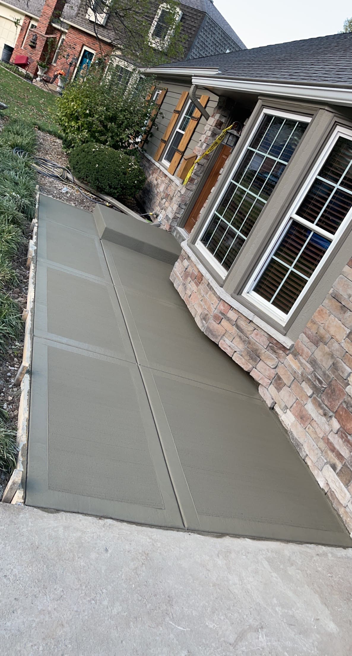 New concrete walkway running alongside a stone-and-siding home