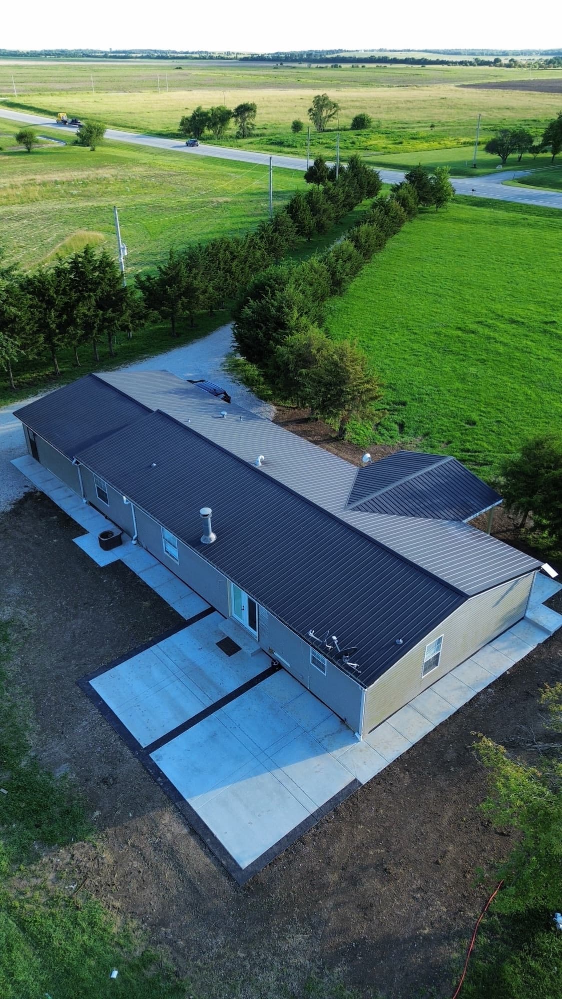Aerial oblique view of a metal-roofed shop building with a large concrete apron, surrounded by grass and farmland
