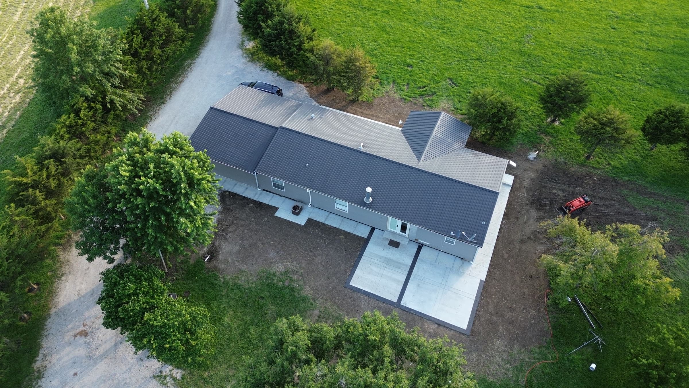 Aerial drone view of a rural metal-roof home with a newly poured concrete patio and approach, surrounded by farmland