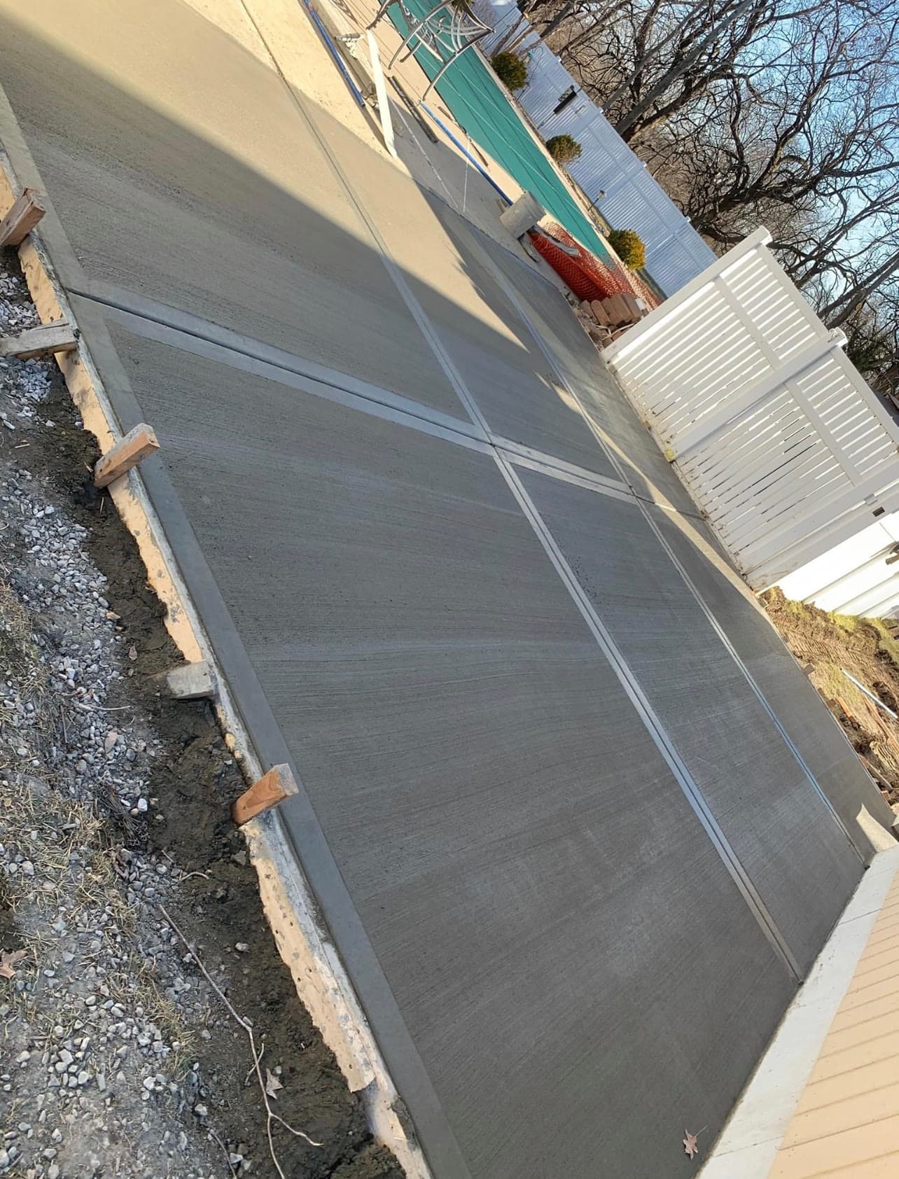 New concrete patio area next to a backyard pool, white vinyl fence and pool cover visible