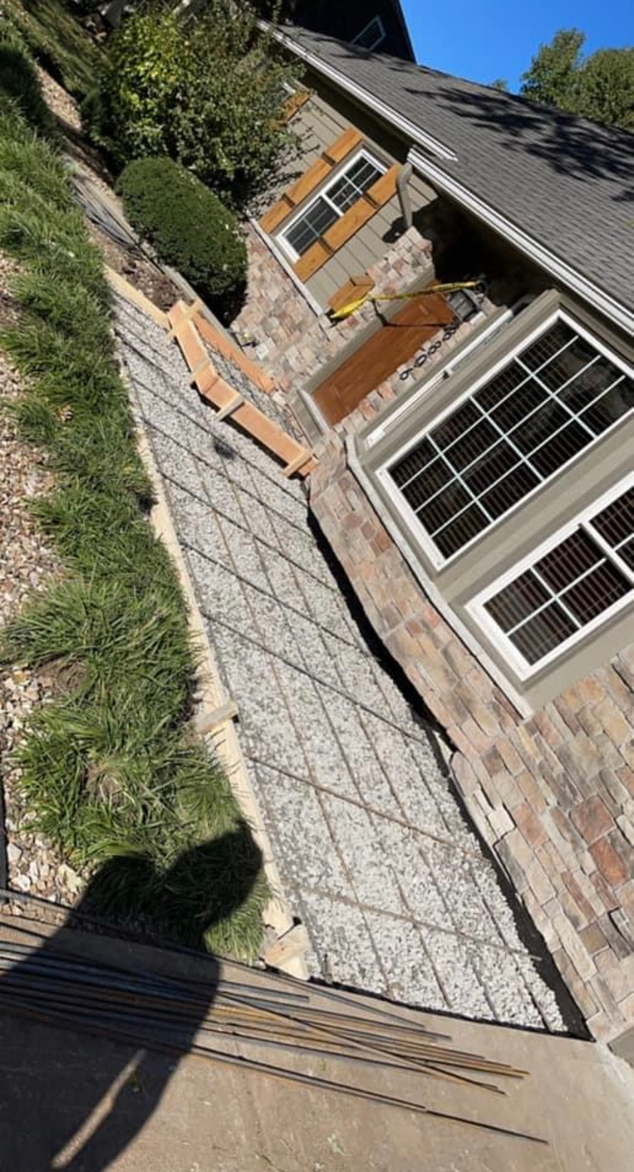 Rebar grid laid over a compacted gravel base, ready for a concrete pour alongside a home