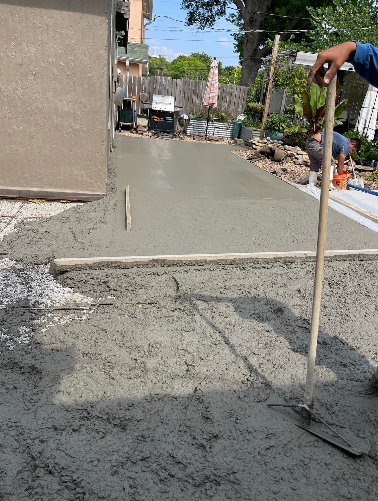 Crew member hand-finishing freshly placed concrete in a backyard section of the shared driveway