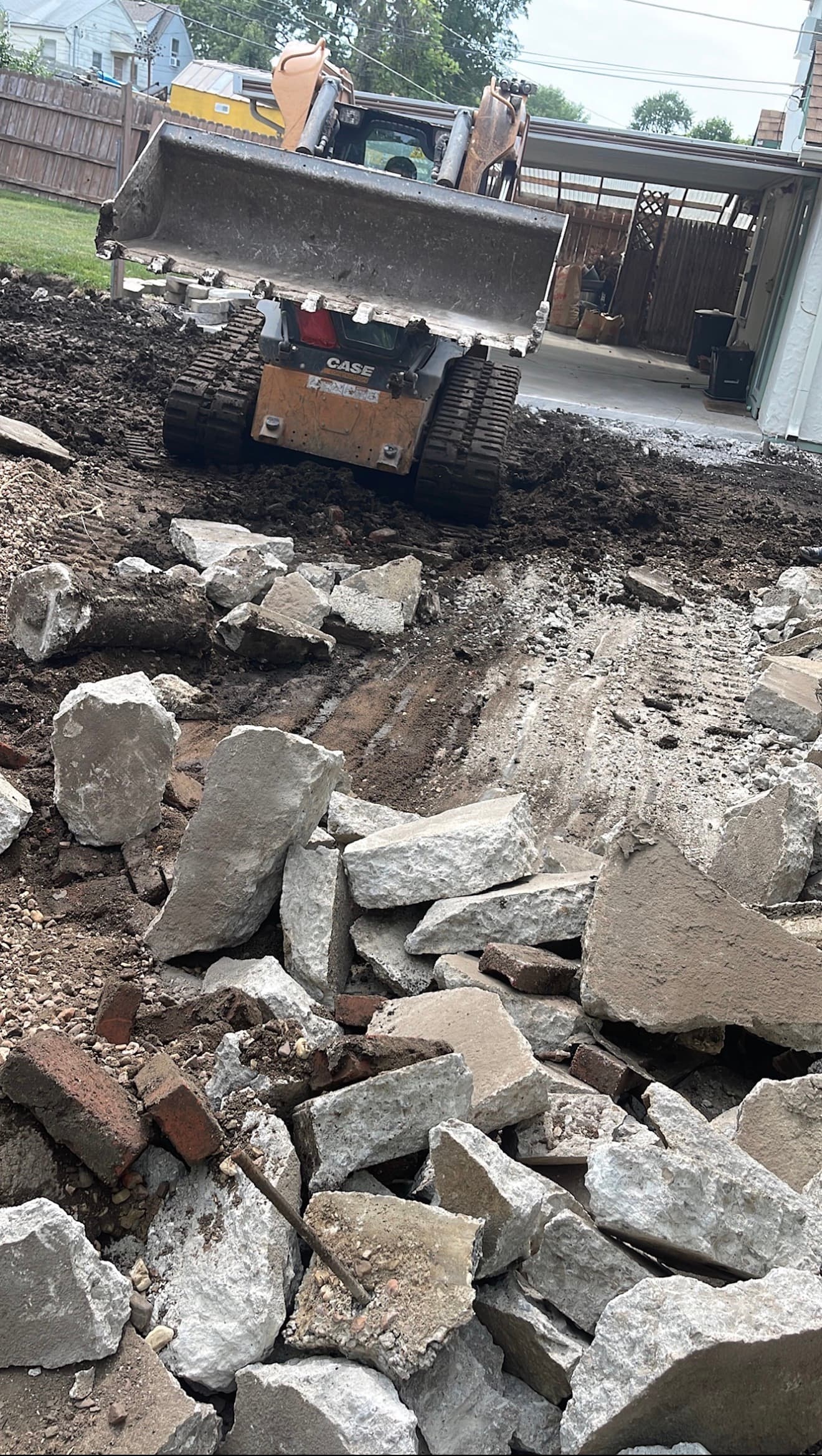 Skid-steer clearing broken concrete and debris along the shared driveway corridor during demolition