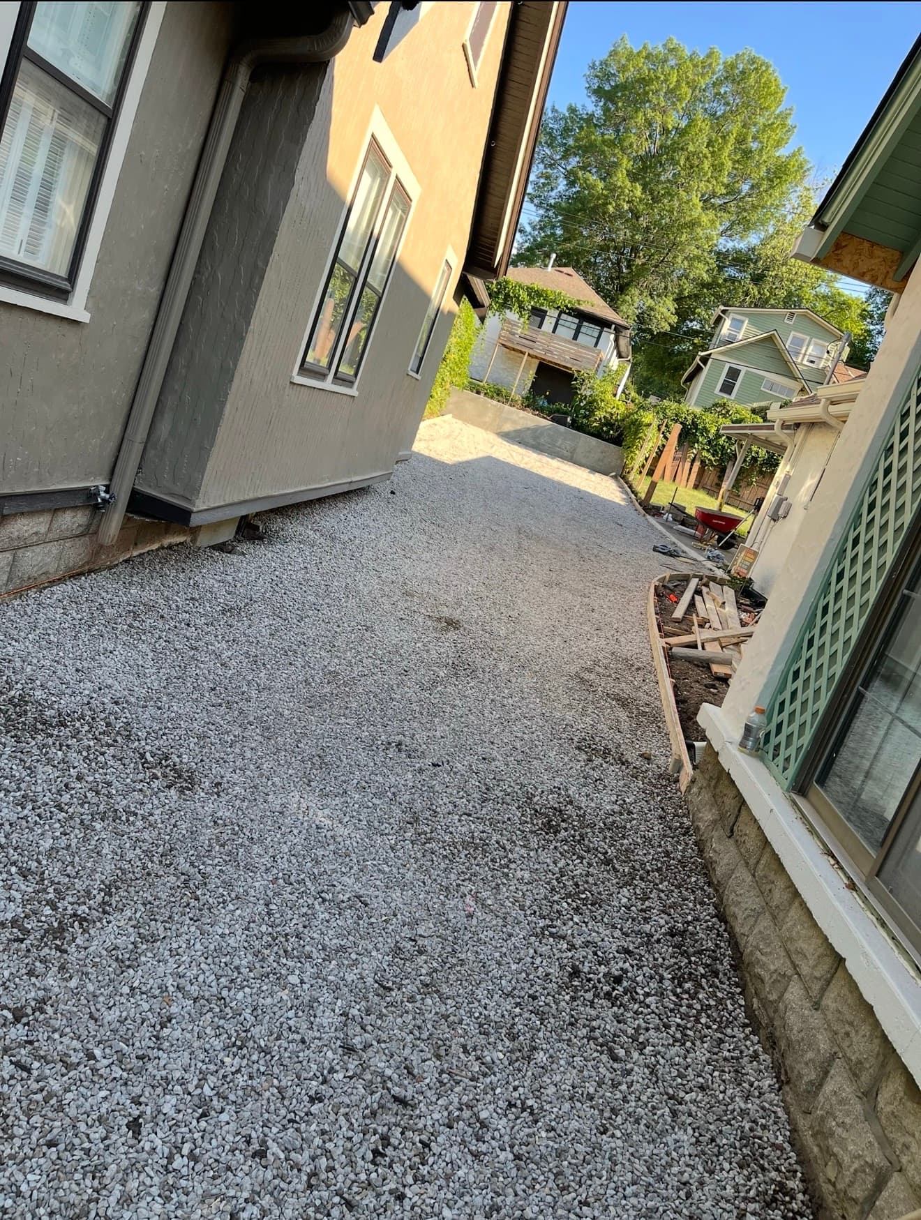 Compacted gravel base prepared for the driveway corridor, with the completed retaining wall visible in the background