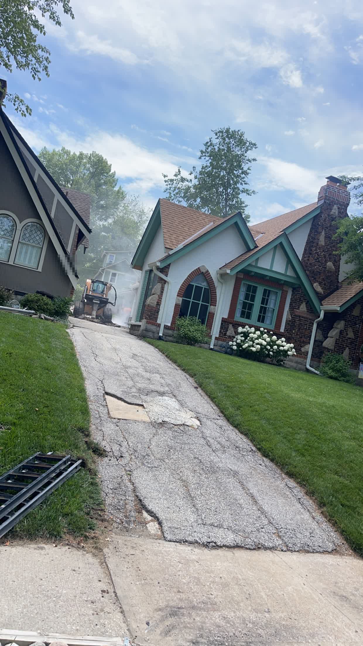 Deteriorated shared concrete driveway with visible cracking and a patched section, running between two houses, before replacement