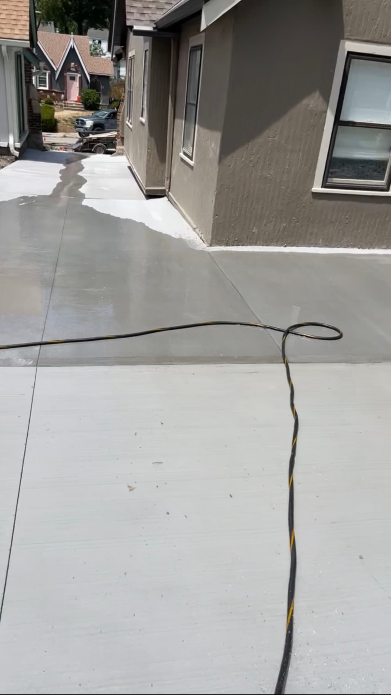 Water introduced onto the finished driveway near the house wall, beginning to spread across the surface
